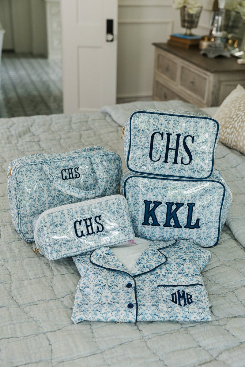 Blue floral pajama and toiletry set with multiple monogrammed travel bags arranged on bedspread.