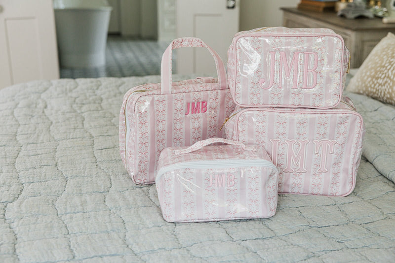 Pink striped monogrammed hanging toiletry bag set with various sizes stacked on a quilted bedspread.