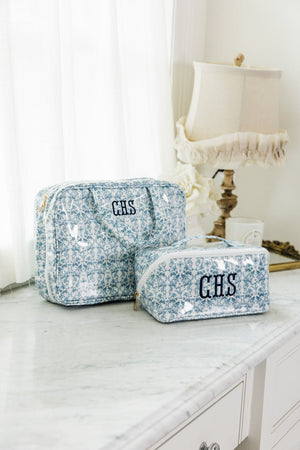 Blue floral hanging toiletry bag set with monogram detail, displayed on marble vanity beside vintage lamp.