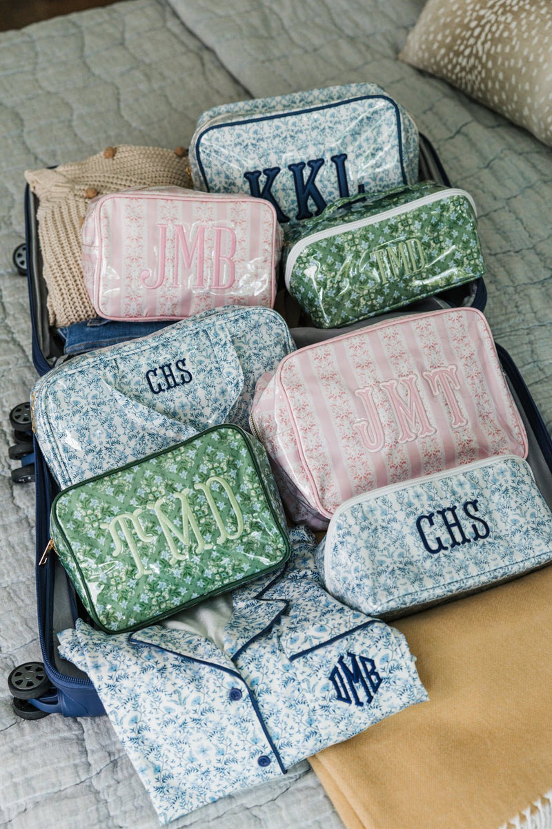 Open suitcase packed with monogrammed toiletry bags in pink, blue, and green floral prints, paired with matching pajamas.