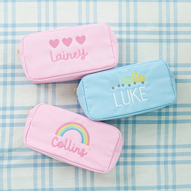 Personalized pouches in pastel colors featuring embroidered names 'Lainey,' 'Luke,' and 'Collins' 