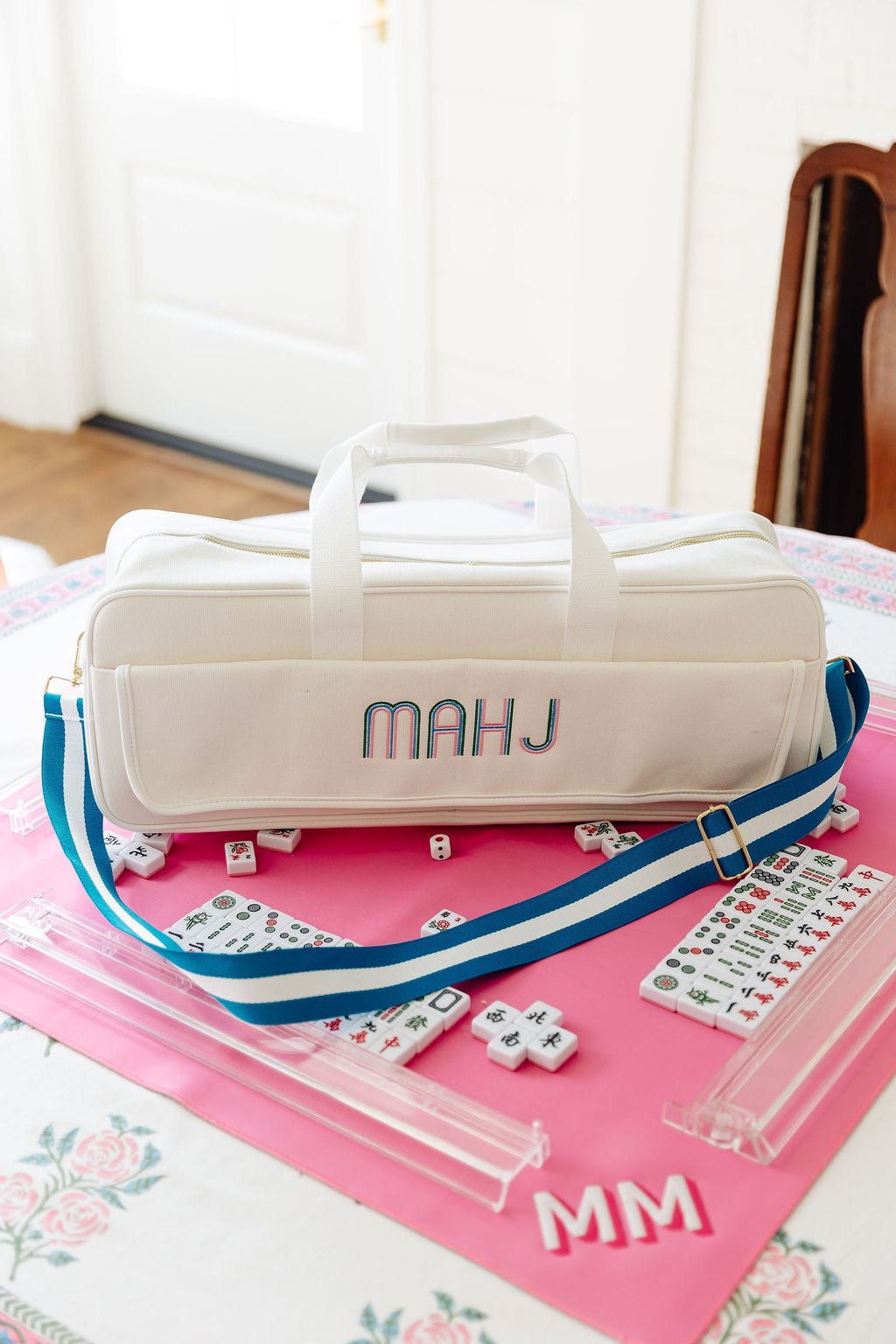 White canvas mahjong carryall duffel with pink trim monogrammed "TM" in blue and pink, with a matching pink and white striped strap