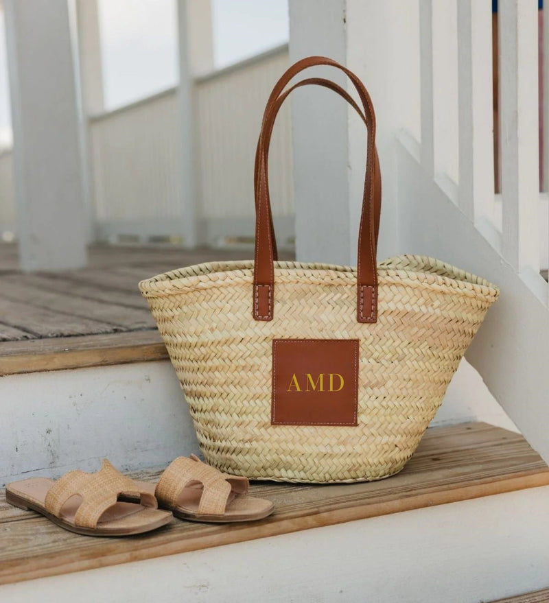 A straw tote on a step is customized with a gold monogram.