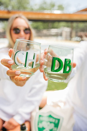 Two people cheers with green monogrammed wine glasses.