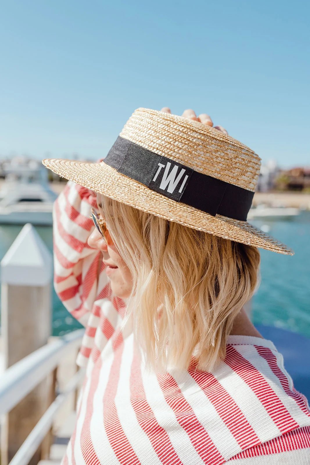 Close-up of a Monogrammed Boater Hat featuring a wide, woven straw brim and a sleek black grosgrain ribbon embroidered with white "KL" initials—perfect for personalized sun protection with a timeless, coastal-chic look.