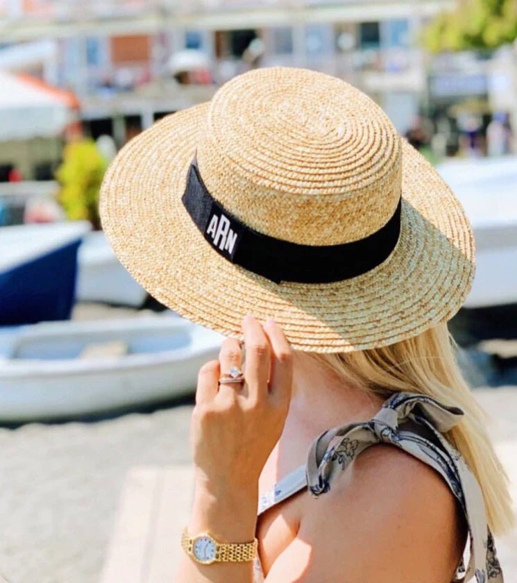 Woman enjoying a sunny day by the water wearing a chic Monogrammed Boater Hat featuring the initials "ARN" embroidered on a black ribbon band, pairing coastal style with personal flair.