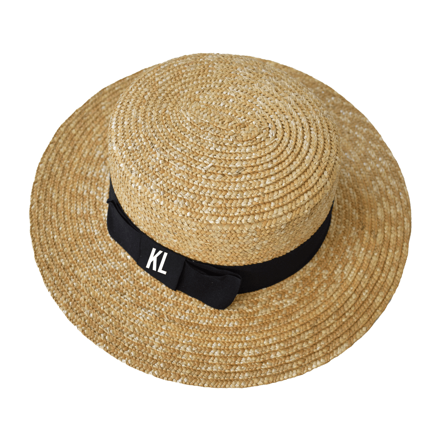 Close-up of a Monogrammed Boater Hat featuring a wide, woven straw brim and a sleek black grosgrain ribbon embroidered with white 