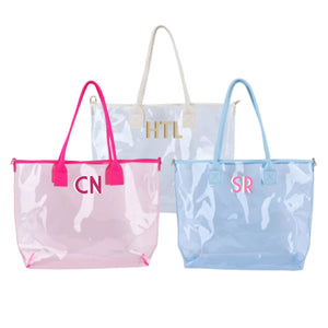 A white, pink, and a blue clear tote are personalized with different colored monograms.