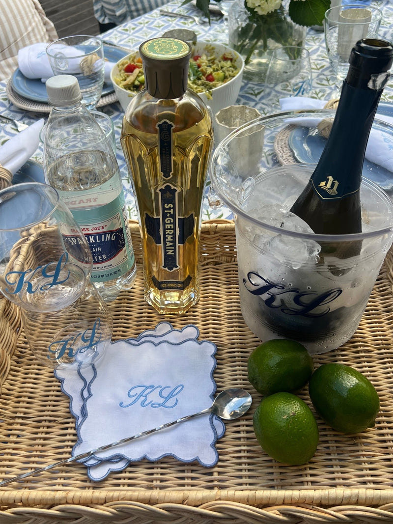 Elegant summer cocktail setup featuring Sprinkled With Pink's Embroidered Monogram Scalloped Cocktail Napkins (Set of 4), adorned with delicate blue scalloped edges and custom "KL" embroidery—perfectly paired with matching monogrammed glassware and an ice bucket for a personalized outdoor celebration.