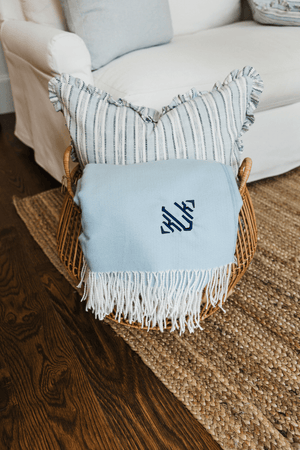 Monogrammed Woven Blanket in light blue with navy initials, folded neatly in wicker basket.