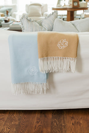 Blue and camel Monogrammed Woven Blankets draped over sofa with embroidered initials and fringe.
