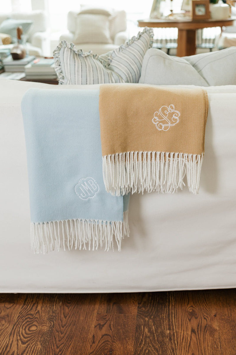 Blue and camel Monogrammed Woven Blankets draped over sofa with embroidered initials and fringe.