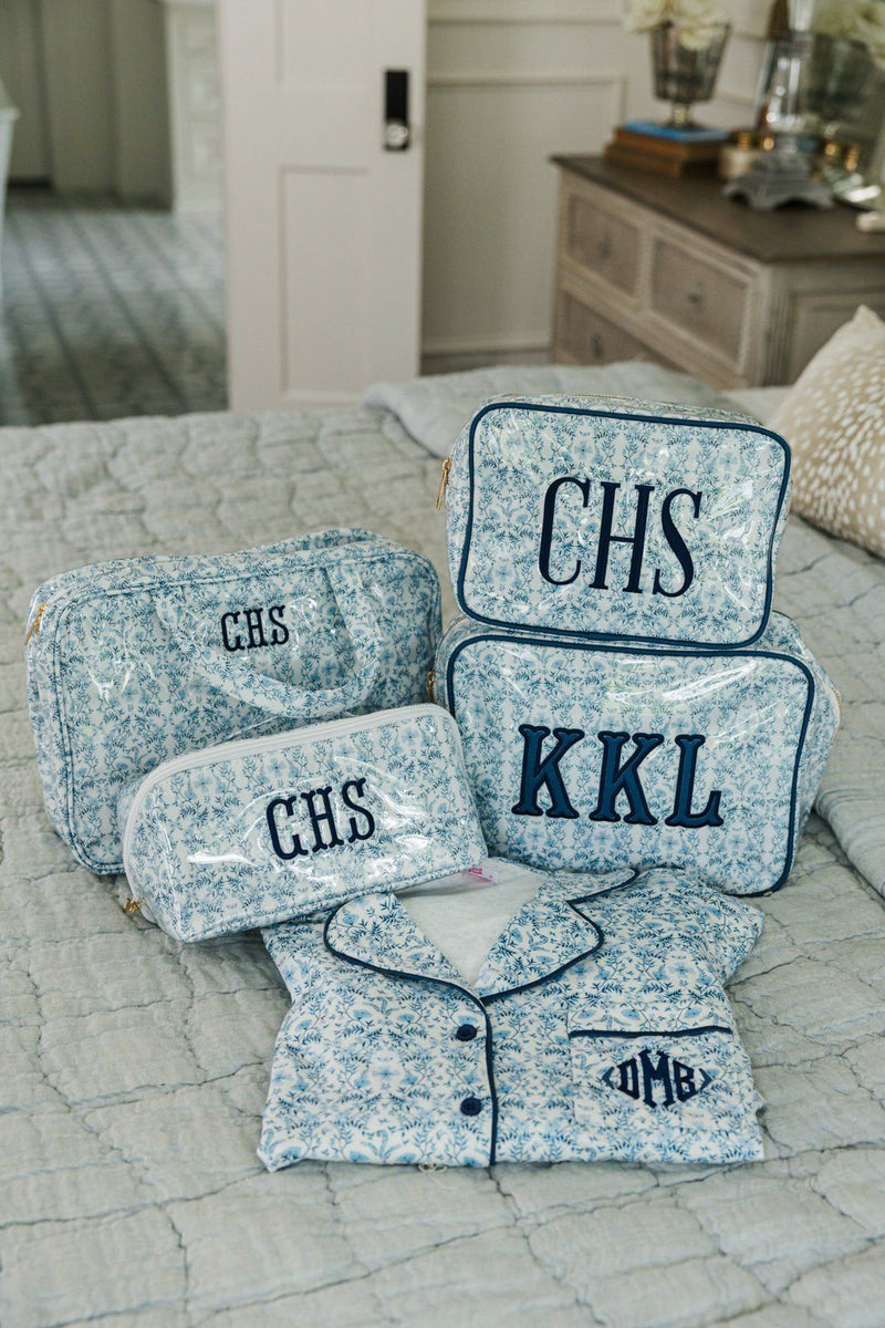 Blue floral pajama set folded neatly with coordinating monogrammed pouches on a quilted bed.