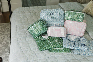 Flat lay of green and blue floral pajama sets paired with matching monogrammed travel pouches.