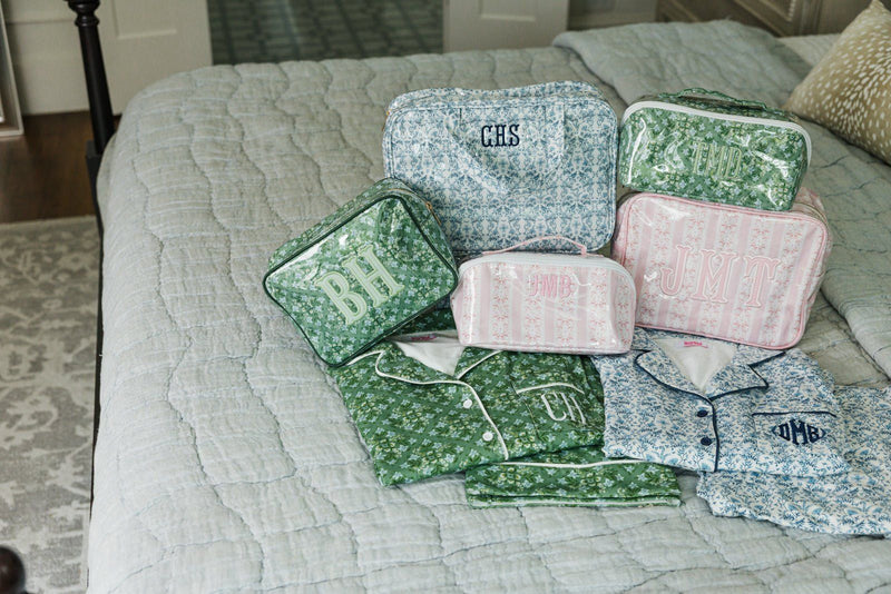 Flat lay of green and blue floral pajama sets paired with matching monogrammed travel pouches.