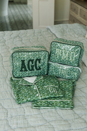Folded green floral pajama set paired with matching monogrammed travel pouches on a bed.
