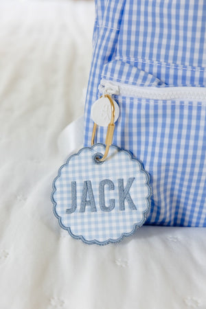 Blue backpack with a gold carabeener and bag tag on the zipper pull that says Jack.