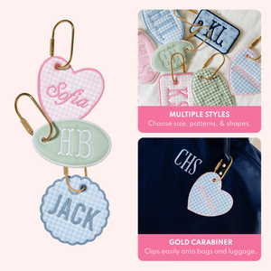 Close-up of assorted bag tags in multiple shapes and patterns, and a heart-shaped blue gingham bag tag embroidered 'emma' clipped to a navy duffel monogrammed 'CHS', with text describing multiple styles and a gold carabiner that clips onto bags and luggage.