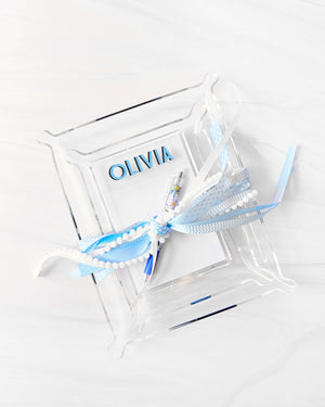 A large acrylic tray, small acrylic tray, and an acrylic notepad holder are nested into each other and held together with a blue and white bow with a pen in it.