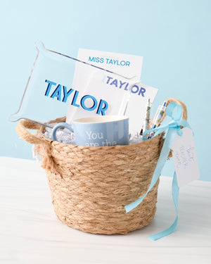 A basket is filled with blue customized products including notepads and an acrylic tray with names on them.
