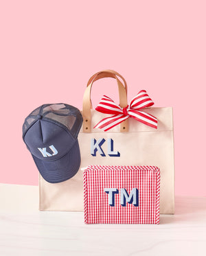 A monogrammed weekender hold a navy monogrammed hat and is placed next to a red monogrammed roadie.