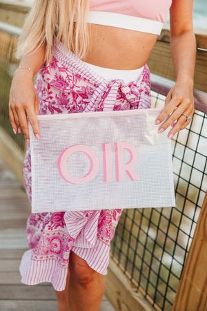 A girl on a board walk holds up a white pool bag with a pink monogram.