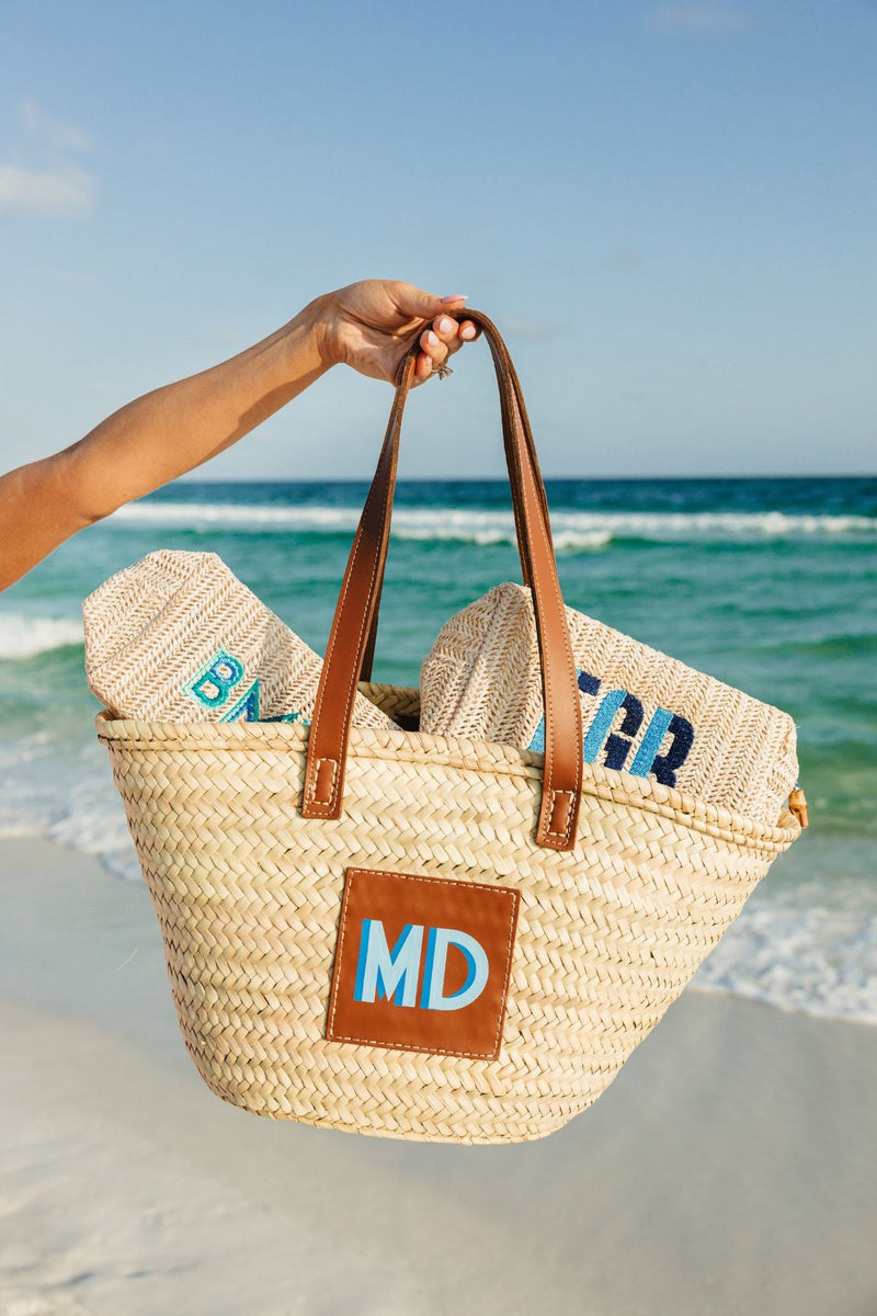A person holds up their straw tote which is holding two straw pouches inside at the beach
