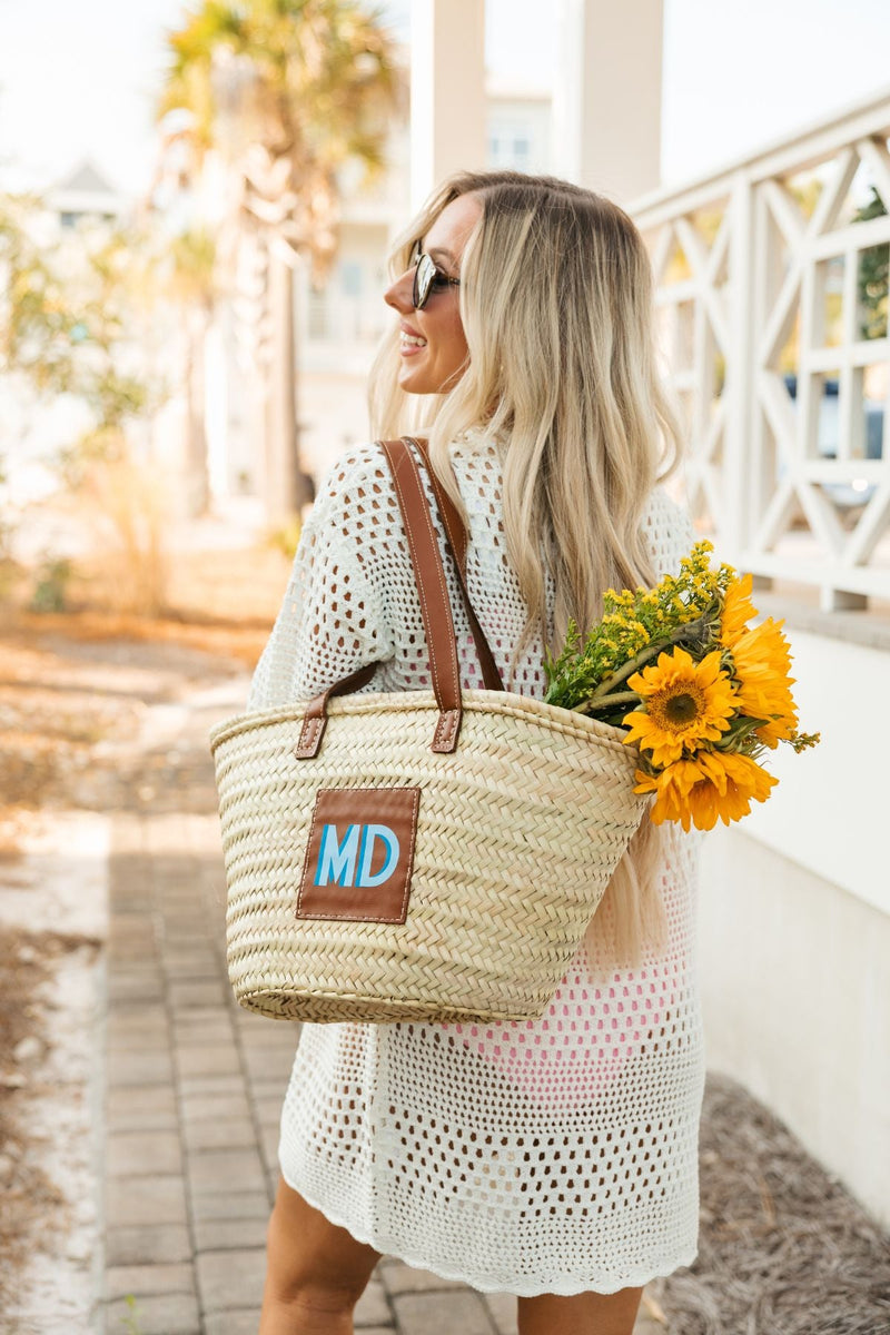 A girl holds a straw tote with a blue monogram and yellow flowers inside.