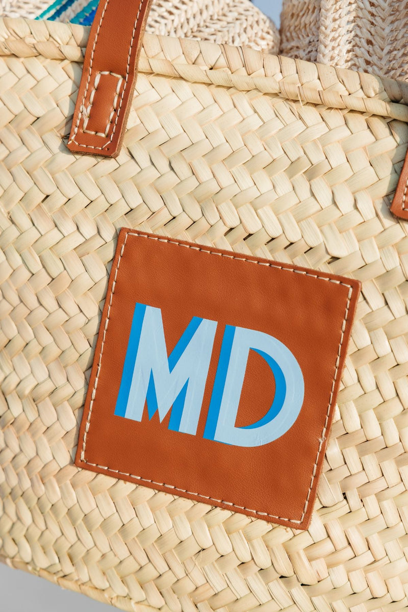 A straw tote is customized with a blue monogram