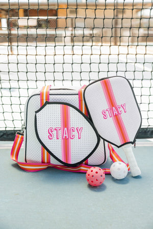 A pink and white pickleball bag and paddle cover are embroidered with matching names.
