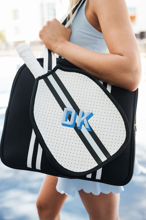 A woman holds a monogrammed black and silver striped pickleball bag on her shoulder 