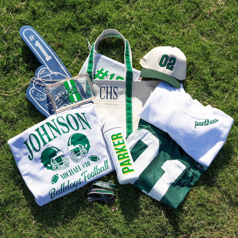 Clear stadium bag with green-white-green stripe, bold “GB” monogram on front, and gold chain shoulder strap.