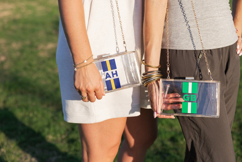 Clear stadium bag with green-white vertical stripes, bold navy “GB” monogram and gold chain strap