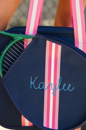 A navy and pink striped tennis bag is customized with a name embroidered in light blue thread.