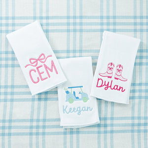 Three personalized towels with embroidered names: 'CEM' with a pink bow, 'Keegan' with a golf cart, and 'Dylan' with cowboy boots.
