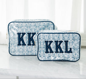 Blue floral XL clear coated pouches with appliqué initials "KKL" styled on marble vanity