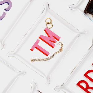 An acrylic tray is customized with a pink monogram and holds gold jewelry.