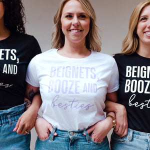 A group of women wear matching shirts that say "beignets, booze, and besties"