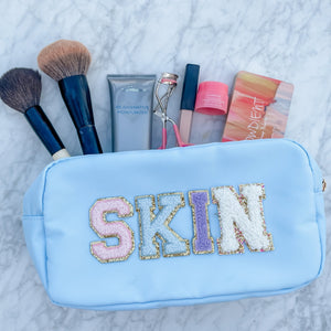 A blue nylon pouch with patches spelling out "SKIN" holds makeup supplies