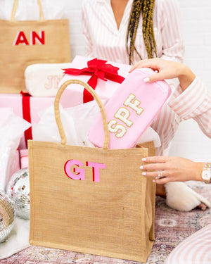 A jute bag is monogrammed with a pink monogram