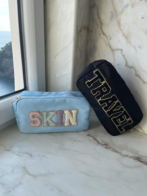 A blue and a black nylon pouch are customized with "Skin" and "Travel" patches