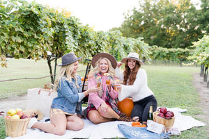 A group of female friends with custom clutches enjoy a picnic at a vineyard