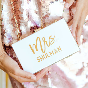 A woman holds a personalized white, acrylic clutch that reads "Mrs. Shulman"