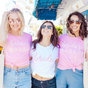 A bride and her two friends laugh as they are styled in "Bride" and "Bride's Babes" Shirts.
