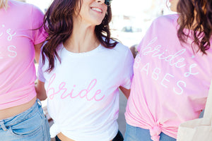 A bride and her two friends laugh as they are styled in "Bride" and "Bride's Babes" Shirts.