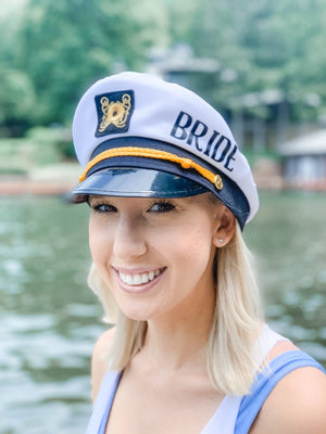 A blonde wears a custom captain's hat that reads "bride" along the side