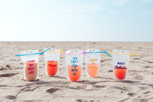 5 party pouches with fun sayings on them sit in the sand at the beach.