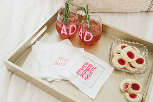 A tray with an assortment of pink cocktail napkins and a monogrammed wine glass.