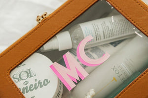 A tan leather toiletry case is personalized with a large pink monogram.