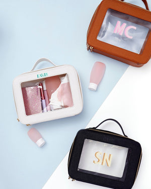 An assortment of clear leather toiletry cases are laid out with different monograms.